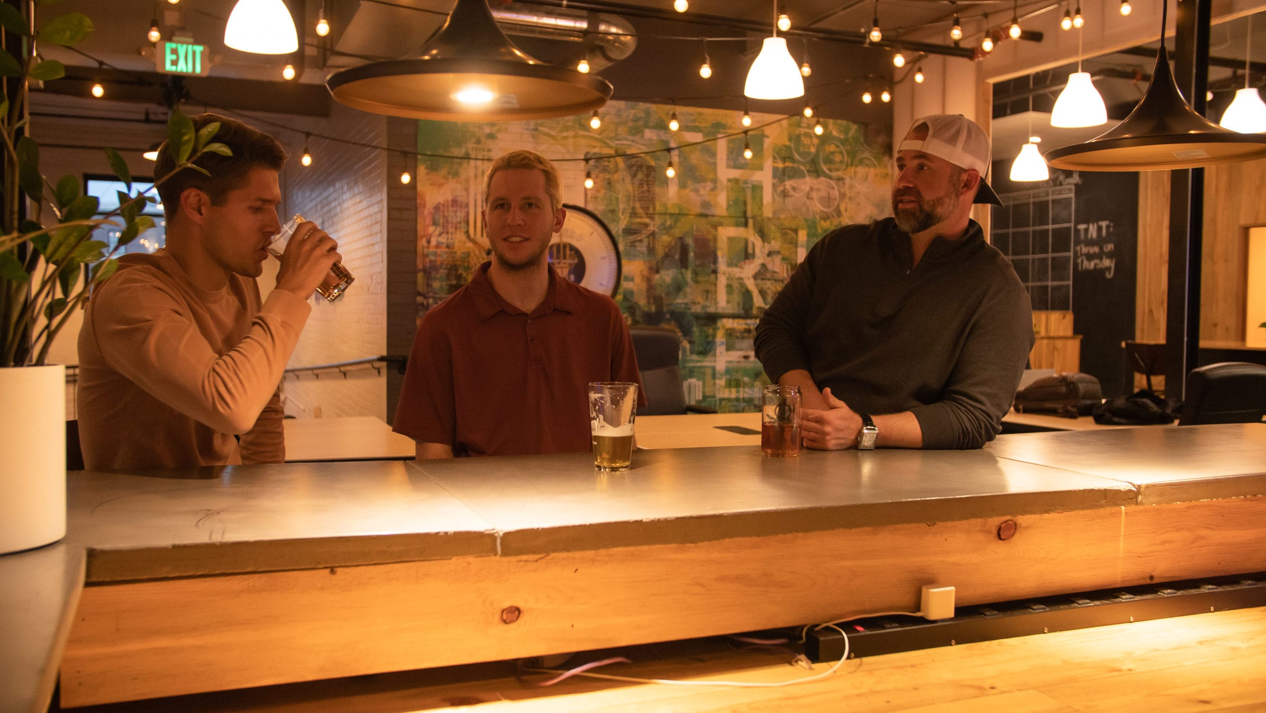 three men standing at a bar with glasses of beer