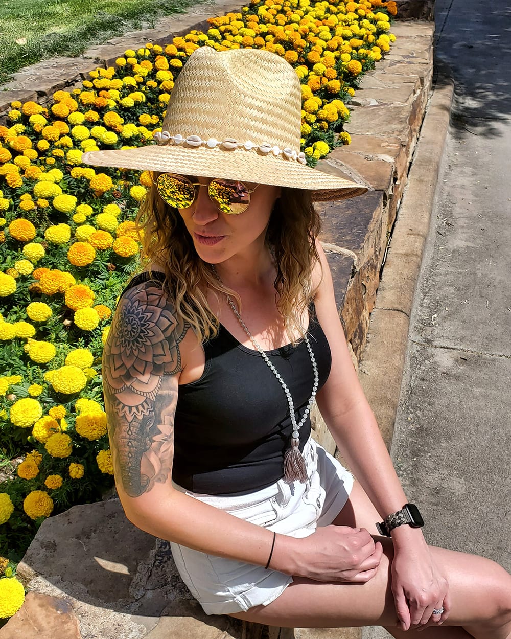 Tara in a hat and sunglasses next to yellow flowers
